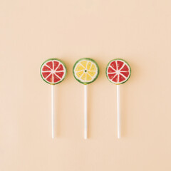 Three fruit lollipops that face on watermelons and limes on a cream background. Candy minimal food summer concept