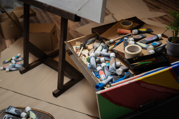 Artist's drawer, painter's cabinet with scattered, disordered paints in tube, painting brushes standing by the easel, artistic mess in the paint store, in the studio.