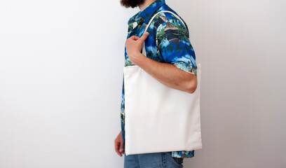 Young man is holding white textile eco bag on white background. Mockup for design