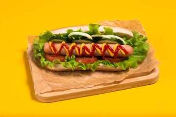 Delicious homemade hot dog with cucumber, tomato and onion. Hot frankfurter. Yellow background. 