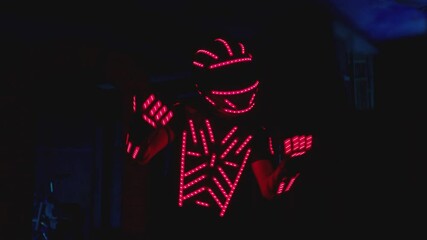 Man dressed in illuminated costume with colorful lights dancing and moving inside dark interior or club . Dancer guy wearing clothing with neon lights on his body and dances . Shot on ARRI camera .