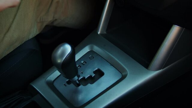 Adult man switching gear lever automatic transmission of a car. Man's hand controlling stick shift transmission. Interior parts of a vehicle