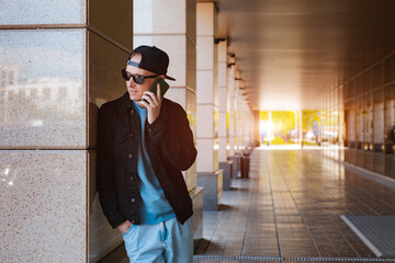 trendy stylish guy black cap sunglasses with smartphone headphones background urban urban sunset