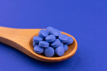 Blue pills in a wooden spoon on a blue background.Copy space.