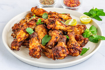 Fototapeta premium Spicy Baked Chicken Wings on a Plate Garnished with Mint Leaves Close Up