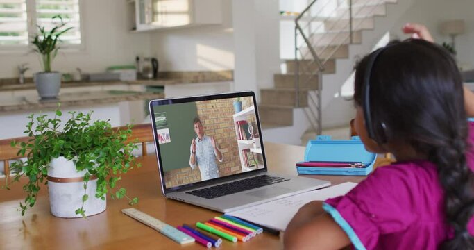 African american girl doing homework while having a video call with male teacher on laptop at home