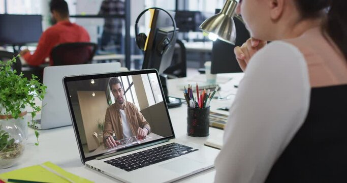 Caucasian woman having a video call with male office colleague on laptop at office