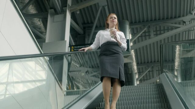 Successful young businesswoman with cup of coffee walks down  escalator in the business center. people goes down the escalator to the subway. An attractive female executive leaves corporate office.