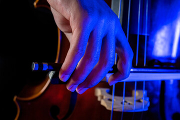 Detail of the right hand holding a cello bow while playing classical music with artistic illumination of blue led light