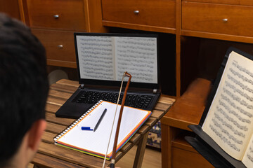 young man taking an online cello lesson with a laptop computer and marking doubtful notes with the...