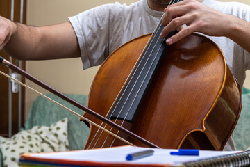 Detail of a teenager playing the classical music instrument Chelo during an online class with a...