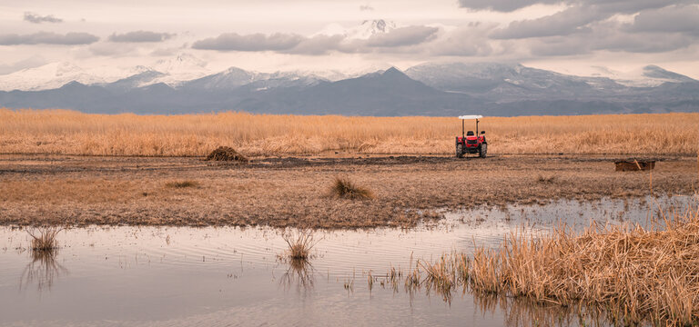 Moody panoramic view of a tractor in front of lake and marshes in Sultan Reedy (Sultansazligi) National Park, central Turkey with snow-capped mountains in the background - Powered by Adobe