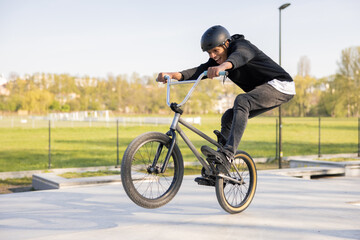 Crazy biker rides his low bike at the skatepark, bmx lifting the front wheel and being in the air...