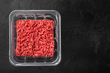 Minced meat in plastic container, on black stone background, top view flat lay, with copy space for...