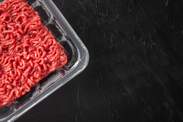 Opened plastic tray with fresh raw minced beef  meat, on black stone background, top view flat lay,...