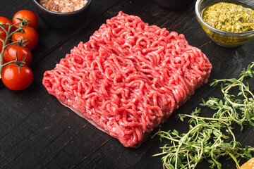 Homemade minced meat in a black bowl with ingredients. Fresh Raw mince for cooking meatballs, on black wooden table background, with copy space for text
