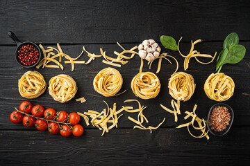 Ingredient of traditional mediterranean cuisine Uncooked pasta tagliatelle, on black wooden table background, top view flat lay, with copy space for text