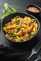 Tasty spicy rabbit stew with pasta tagliatelle or pappardelle, in bowl, on black stone background