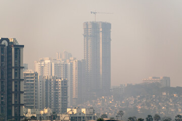A hazy skyline of suburban Mumbai with a highrise skyscraper under construction.