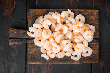 Pile of boiled peeled  shrimps, on wooden serving board, on old dark  wooden table , top view flat...