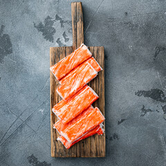 Fresh Crab meat stick surimi with blue swimming crab, on wooden cutting board, on gray background, top view flat lay