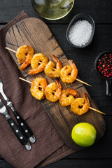 Roasted peeled prawn with skewer, on black wooden table background, top view flat lay