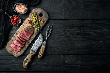 Grilled fillet beef steaks, with onion and asparagus, on wooden serving board, with meat knife and...