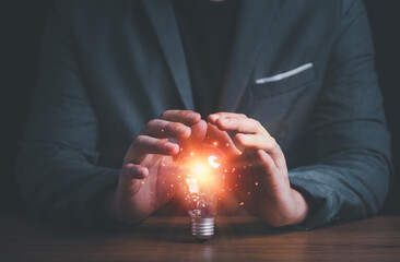 Businessman hand protect lightbulb which orange glowing light ray ,creative innovation idea and...