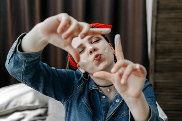 A cheerful brunette with a red bandage in her hair crossed her lips in a kiss and closed her eyes. She extended her arms forward like a viewfinder, fingers crossed. Portrait through the fingers.