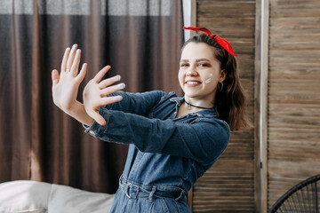 Photo of a cheerful girl with crossed arms. The brunette smiles, looking at the camera, on her head there is a red bandage tied with a bow. There are white spots of paint on the cheeks.