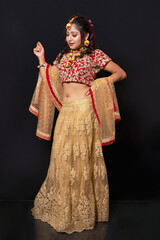 Young attractive Indian female model dressed in traditional Indian lehenga choli costume with Kundan style jewelry. Full length shot. Black background