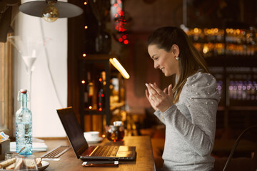 Beautiful young girl woman sitting in a posture cafe smiles and spreads her arms after reading a message