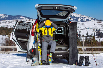 woman dressing in ski equipment while sitting in car trunk.