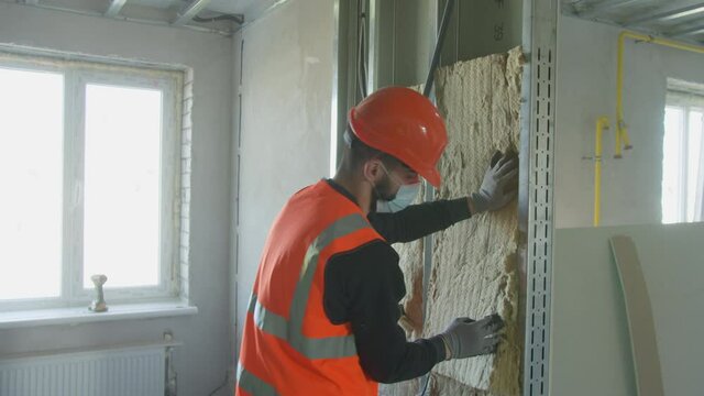 Male builder in mask putting foam into drywall