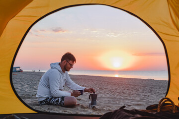 Fototapeta premium man cooking coffee at sea sandy beach. summer camping vacation
