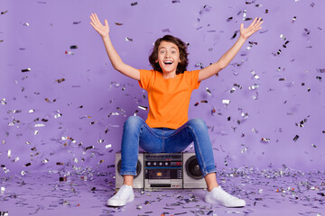 Portrait of attractive cheerful boy sitting on player throwing confetti having fun isolated over...