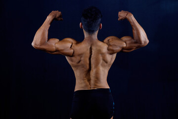Obraz premium Muscular bodybuilder male in gym. Black background. Back profile.Showing arm and back muscles.