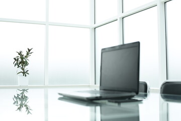 Fototapeta na wymiar Grey laptop on glass table in bright office space