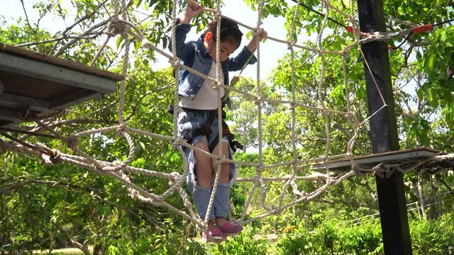 Happy asian Little Girl climbing on rope nets on playground .kid brave adventure