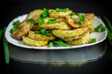 fried zucchini in circles with fresh herbs in a plate on a black