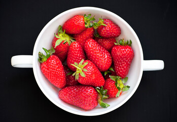 Beautiful red, ripe strawberries placed in a white bowl with stalks. Close up picture on a black background.