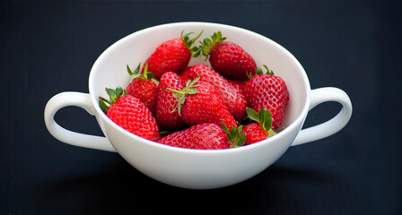 Beautiful red, ripe strawberries placed in a white bowl with stalks. Photo on a black background.
