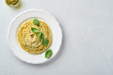 Pasta spaghetti with pesto sauce and fresh basil leaves in white bowl. Grey background.  Mock up. Top view.