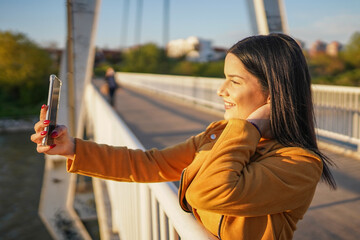 Obraz premium Beautiful woman standing on bridge and making selfie