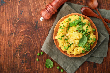 Mashed potato with butter, green peas, onions, basil on a rustic wooden background. Top view with close up.