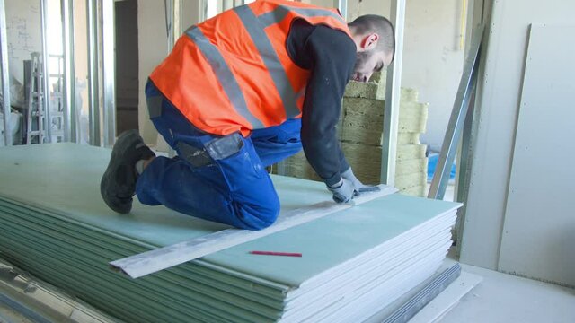 Male builder measuring and cutting gypsum panel