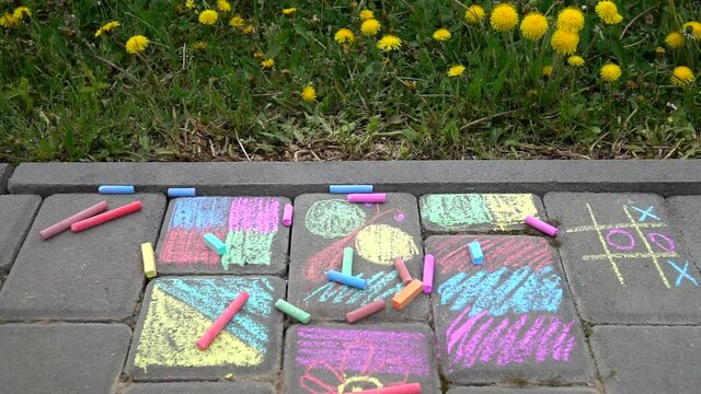 Multicolored crayons falling on the paving slabs with children's drawings against the background of green grass and yellow dandelions, slow motion
