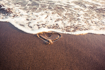 End of love metaphor. Heart drawn on a sand being wiped off with tidal wash.