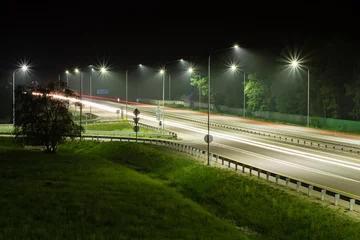 Fotobehang Night highway in the light of streetlights and the plumes of headlights of passing cars © VeNN