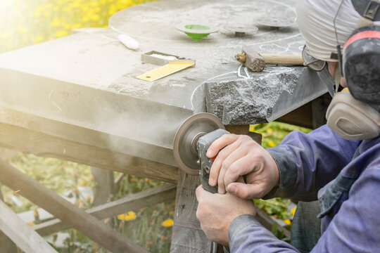 Street lighting. a masked worker processes a granite stone with a special tool. Close-up.